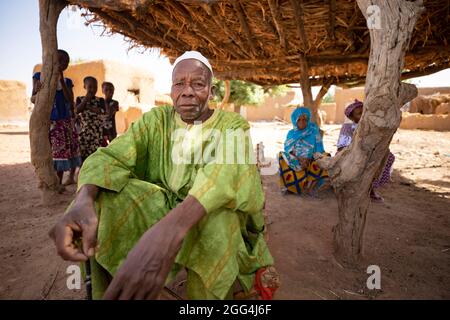 Mahammoud Traore (75) unterstützt eine 21-köpfige Familie durch seine Landwirtschaft im Dorf Dougouninkoro, Mali. Aber der Klimawandel hat die Wettermuster in den letzten Jahren beeinflusst und er konnte nicht so viel wachsen wie früher. Jetzt gehen die Lebensmittelgeschäfte seiner Familie immer aus, bevor er seine neue Ernte ernten kann. Daher gibt es jedes Jahr ein paar Monate, in denen die Familie Hunger hat und sie oft Schulden machen müssen, um Lebensmittel zu kaufen oder sich etwas zu leihen. Sahel-Krise 2021; Barouéli Cercle, Mali. Februar 22, 2021. Foto von Jake Lyell. Stockfoto