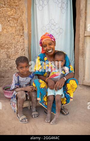 Eine junge alleinerziehende Fulani-Mutter und ihre beiden Töchter sitzen in der Tür ihres Lehmhauses in der Region Ségou, Mali, Westafrika. Stockfoto