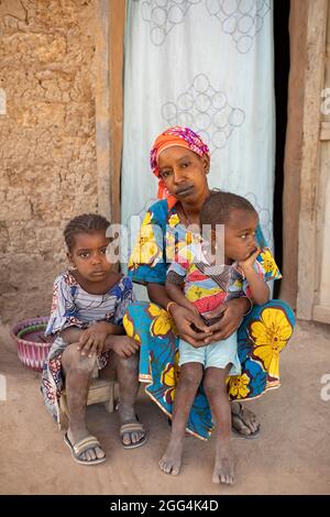 Eine junge alleinerziehende Fulani-Mutter und ihre beiden Töchter sitzen in der Tür ihres Lehmhauses in der Region Ségou, Mali, Westafrika. Stockfoto