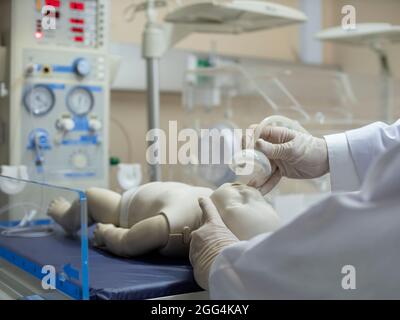 Ein Arzt, der ein Modell eines Neugeborenen mit einer Sauerstoffmaske unter einem Strahlungswärmer/Beatmungsgerät aufsetzt. Stockfoto