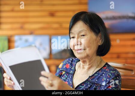 Ältere asiatische Frau lächelt beim Lesen der Zeitschrift Stockfoto