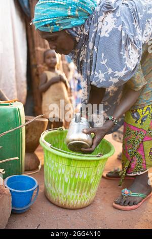 Das Senou Camp liegt am südlichen Rand von Bamako, Malis Hauptstadt. Es ist eines von acht solchen informellen Camps in der ganzen Stadt und allein beherbergt es 223 Familien und etwas mehr als 1.000 Binnenvertriebene. Die hier lebenden Familien sind vor Gewalt und Aufstand im Norden und in den zentralen Teilen des Landes geflohen. Da die meisten von ihnen kein Einkommen oder eine regelmäßige Nahrungsquelle haben, ist der Hunger eine tägliche Herausforderung und die Unterernährung der Bevölkerung ist nach wie vor weit verbreitet. Hier wäscht Miriam Barry morgens einen Topf, während sie für ihre Familie außerhalb ihres provisorischen Tierheims das Frühstück kocht. Stockfoto