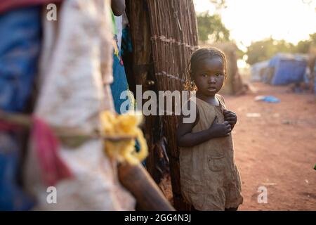Das Senou Camp liegt am südlichen Rand von Bamako, Malis Hauptstadt. Es ist eines von acht solchen informellen Camps in der ganzen Stadt und allein beherbergt es 223 Familien und etwas mehr als 1.000 Binnenvertriebene. Die hier lebenden Familien sind vor Gewalt und Aufstand im Norden des Landes geflohen. Da die meisten von ihnen kein Einkommen oder eine regelmäßige Nahrungsquelle haben, ist der Hunger eine tägliche Herausforderung und die Unterernährung der Bevölkerung ist nach wie vor weit verbreitet. Hier steht Djeneba Barry (3) vor dem provisorischen Tierheim ihrer Familie. Stockfoto