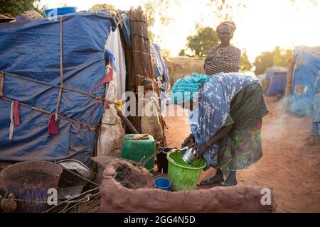 Das Senou Camp liegt am südlichen Rand von Bamako, Malis Hauptstadt. Es ist eines von acht solchen informellen Camps in der ganzen Stadt und allein beherbergt es 223 Familien und etwas mehr als 1,000 Binnenvertriebene. Die hier lebenden Familien sind vor Gewalt und Aufstand im Norden und in den zentralen Teilen des Landes geflohen. Da die meisten von ihnen kein Einkommen oder eine regelmäßige Nahrungsquelle haben, ist der Hunger eine tägliche Herausforderung und die Unterernährung der Bevölkerung ist nach wie vor weit verbreitet. Hier wäscht Miriam Barry morgens einen Topf, während sie für ihre Familie außerhalb ihres provisorischen Tierheims das Frühstück kocht. Sahel-Krise 2021; Senou, Mali. Stockfoto
