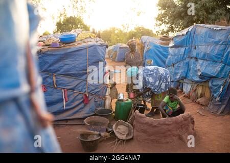 Das Senou Camp liegt am südlichen Rand von Bamako, Malis Hauptstadt. Es ist eines von acht solchen informellen Camps in der ganzen Stadt und allein beherbergt es 223 Familien und etwas mehr als 1,000 Binnenvertriebene. Die hier lebenden Familien sind vor Gewalt und Aufstand im Norden und in den zentralen Teilen des Landes geflohen. Da die meisten von ihnen kein Einkommen oder eine regelmäßige Nahrungsquelle haben, ist der Hunger eine tägliche Herausforderung und die Unterernährung der Bevölkerung ist nach wie vor weit verbreitet. Hier wäscht Miriam Barry morgens Gerichte, während sie für ihre Familie außerhalb ihres provisorischen Tierheims das Frühstück kocht. Sahel-Krise 2021; Senou, Mali Stockfoto