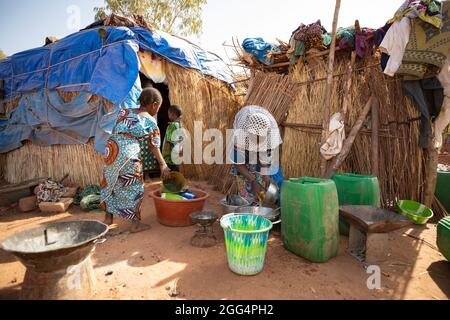 Das Senou Camp liegt am südlichen Rand von Bamako, Malis Hauptstadt. Es ist eines von acht solchen informellen Camps in der ganzen Stadt und allein beherbergt es 223 Familien und etwas mehr als 1.000 Binnenvertriebene. Die hier lebenden Familien sind vor Gewalt und Aufstand im Norden und in den zentralen Teilen des Landes geflohen. Da die meisten von ihnen kein Einkommen oder eine regelmäßige Nahrungsquelle haben, ist der Hunger eine tägliche Herausforderung und die Unterernährung der Bevölkerung ist nach wie vor weit verbreitet. Hier wäscht Fatima Bolly (33) mit zwei ihrer Kinder vor dem provisorischen Tierheim ihrer Familie Geschirr. Stockfoto