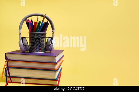 Zurück zu den Schulkonzepten. Lehrertag. Komposition aus einem Stapel von Büchern Bleistifte Brille kabellose Kopfhörer auf einem gelben Hintergrund mit Kopierfläche Stockfoto