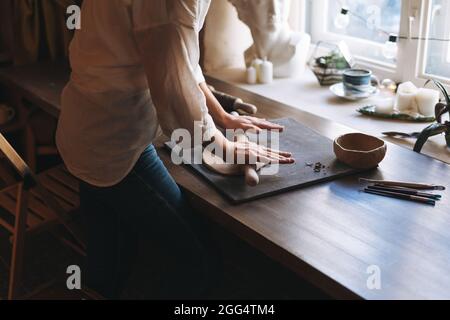 Junge attraktive Frau in weißem Hemd Keramik Künstler Dekoration Tonplatte mit Werkzeug am Tisch in Keramik-Werkstatt. Handgemachte Arbeit Student, Hobbys und Stockfoto