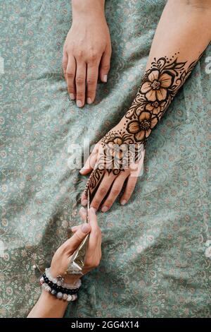 Künstlerin, die Henna-Tätowierung auf Frauenhänden anwendet. Mehndi ist traditionelle indische dekorative Kunst, Hand mit floralen Mehendi. Beauty-Zeichnung für Hochzeiten und Stockfoto