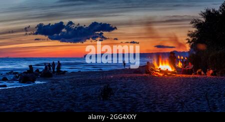 Nicht erkennbare Menschen feiern Sommersonnenwende mit Lagerfeuer am Strand Stockfoto