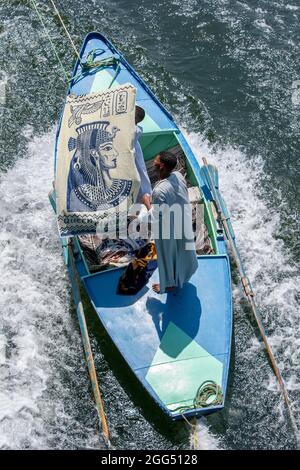 Ein Textilverkäufer an Bord eines Ruderbootes versucht, Touristen auf einem schwimmenden Hotelschiff, das von Luxor nach Esna in Ägypten fährt, ein beschriftete Tuch zu verkaufen. Stockfoto