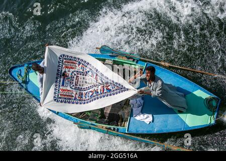 Textilverkäufer an Bord eines Ruderbootes, der von einem schwimmenden Hotelschiff auf dem Nil von Luxor nach Esna in Ägypten geschleppt wird. Stockfoto