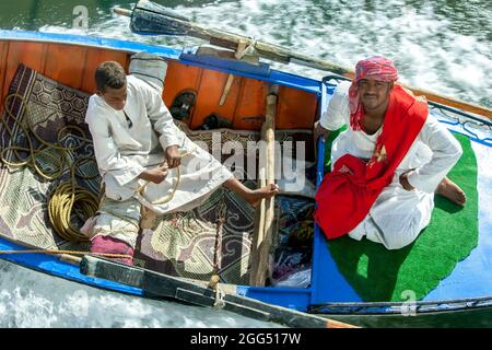 Textilverkäufer an Bord eines Ruderbootes, der von einem schwimmenden Hotelschiff auf dem Nil von Luxor nach Esna in Ägypten geschleppt wird. Stockfoto