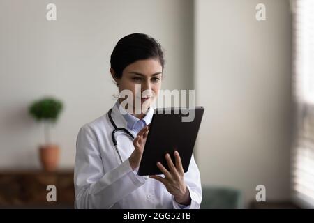 Konzentrierte junge indische Ärztin mit digitaler Tablette. Stockfoto