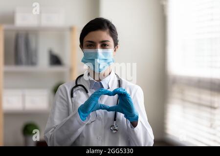 Glücklicher junger indischer Arzt, der Herzzeichen zeigt. Stockfoto