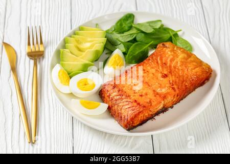 Im Ofen gebackenes Lachsfilet mit cremig reifer Avocado, Babyspinat und hart gekochten Eiern auf einem weißen Teller Stockfoto