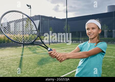 Schönes Kind in Sportswear mit Tennisschläger, während es Tennis auf dem Tennisplatz spielt. Kleines Mädchen Tennisspielerin Stockfoto