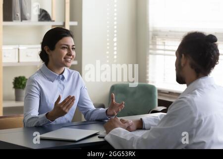 Lächelnder indischer Patient im Gespräch mit einem afrikanischen Arzt. Stockfoto