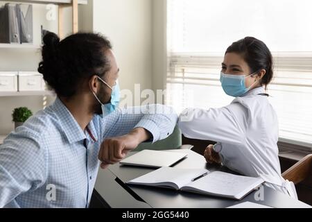 Glücklicher junger gemischter Rassenpatient und Arzt, der Ellbogen berührt. Stockfoto