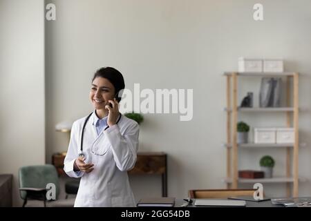 Lächelnd freundliche junge indische Ärztin, die ein Telefongespräch hält. Stockfoto