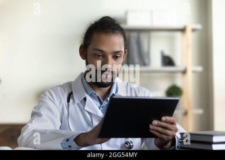 Konzentrierter junger afroamerikanischer Arzt mit digitaler Tablette. Stockfoto