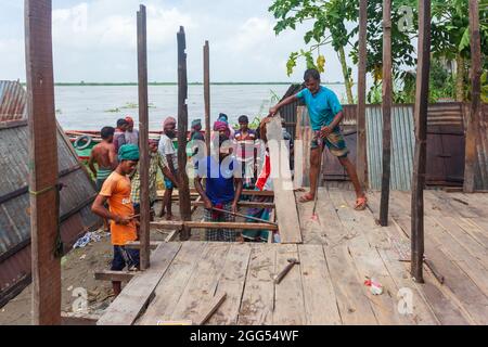 Munshiganj, Bangladesch. August 2021. Arbeiter tragen Holzteile aus einem beschädigten Haus, da die Erosion des Flusses Padma die Betonstrukturen in Tongibari, Munshiganj, am Stadtrand von Dhaka, weiter wegspült.nach dem Monsun haben sich gewaltsame Erosionen in die Ufer des Padma-Flusses gefressen, die große Teile in Munshiganj, Tongibari Upazila, Bangladesch, bedrohten. Kredit: SOPA Images Limited/Alamy Live Nachrichten Stockfoto