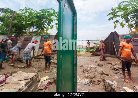 Munshiganj, Bangladesch. August 2021. Arbeiter tragen Holzteile aus einem beschädigten Haus, da die Erosion des Flusses Padma die Betonstrukturen in Tongibari, Munshiganj, am Stadtrand von Dhaka, weiter wegspült.nach dem Monsun haben sich gewaltsame Erosionen in die Ufer des Padma-Flusses gefressen, die große Teile in Munshiganj, Tongibari Upazila, Bangladesch, bedrohten. Kredit: SOPA Images Limited/Alamy Live Nachrichten Stockfoto