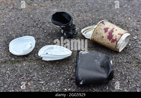 Zerknittert eine Papierkaffeetasse auf Asphalt. Weggeworfene Einweg-Kaffeetasse mit Kunststoffdeckel auf der Straße. Becher aus zerkleinertem Papier. Abgebrochener Müll Stockfoto