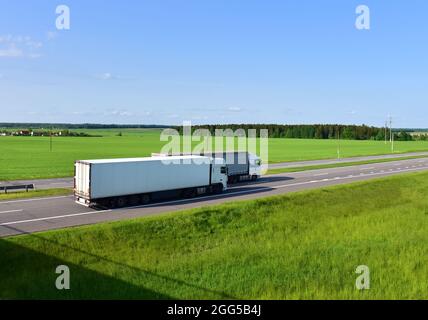 LKW auf einer asphaltierten Straße überholt einen anderen LKW. Lastwagen mit Sattelaufliegern fahren entlang der Autobahn. Warenlieferung auf der Straße. Dienstleistungen und Transport logi Stockfoto