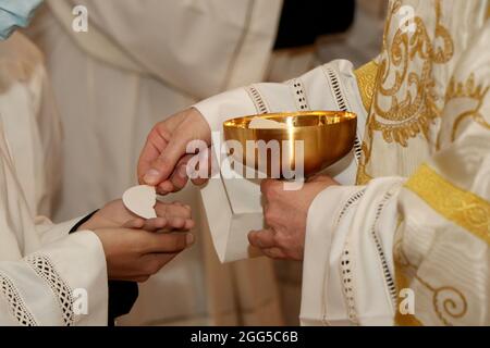 Kommunion Ritus während der Messe in einer katholischen Kirche. Priester geben Gastgeber in den Händen eines Gläubigen Stockfoto