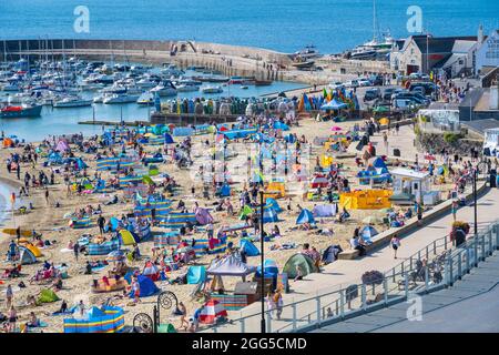 Lyme Regis, Dorset, Großbritannien. August 2021. Wetter in Großbritannien: Urlauber und Familien strömen an den beliebten Strand am Badeort Lyme Regis, um am Feiertagswochenende die glühend heiße Sonne und den klaren blauen Himmel zu genießen. Angesichts des herrlichen Sonnenwetters, das bis zum Montag an den Bankfeiertagen andauern wird, werden die Strände und Resorts an der Südküste voraussichtlich noch stärker überfüllt sein als sonst, da in diesem Sommer mehr Menschen in Großbritannien Urlaub machen. Der Kredit: Celia McMahon/Alamy Live Nachrichten Stockfoto
