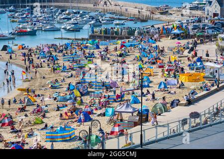 Lyme Regis, Dorset, Großbritannien. August 2021. Wetter in Großbritannien: Urlauber und Familien strömen an den beliebten Strand am Badeort Lyme Regis, um am Feiertagswochenende die glühend heiße Sonne und den klaren blauen Himmel zu genießen. Angesichts des herrlichen Sonnenwetters, das bis zum Montag an den Bankfeiertagen andauern wird, werden die Strände und Resorts an der Südküste voraussichtlich noch stärker überfüllt sein als sonst, da in diesem Sommer mehr Menschen in Großbritannien Urlaub machen. Der Kredit: Celia McMahon/Alamy Live Nachrichten Stockfoto