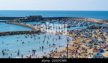 Lyme Regis, Dorset, Großbritannien. August 2021. Wetter in Großbritannien: Urlauber und Familien strömen an den beliebten Strand am Badeort Lyme Regis, um am Feiertagswochenende die glühend heiße Sonne und den klaren blauen Himmel zu genießen. Angesichts des herrlichen Sonnenwetters, das bis zum Montag an den Bankfeiertagen andauern wird, werden die Strände und Resorts an der Südküste voraussichtlich noch stärker überfüllt sein als sonst, da in diesem Sommer mehr Menschen in Großbritannien Urlaub machen. Der Kredit: Celia McMahon/Alamy Live Nachrichten Stockfoto