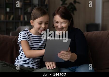 Glückliches kleines Mädchen mit Tablet mit älteren Oma. Stockfoto