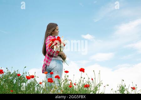 Blumenstrauß: Mohnblumen, Gänseblümchen in der Hand gegen den blauen Himmel. Blumen in der Hand einer Frau Stockfoto