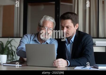 Selbstbewusster, reifer Geschäftsmann, Mentor, der neue Mitarbeiter mit einem Laptop ausbilden kann Stockfoto