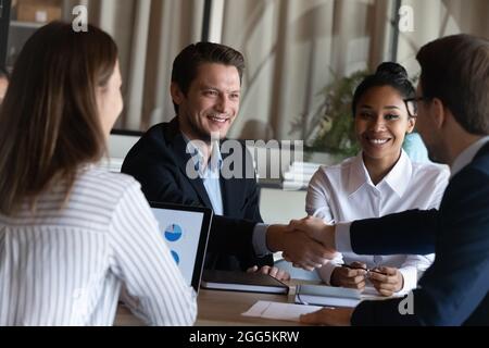 Lächelnde Geschäftspartner schütteln bei Gruppenverhandlungen die Hände Stockfoto
