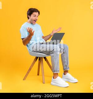 Aufgeregt Kerl mit Laptop feiert Erfolg sitzen auf einem Stuhl Stockfoto