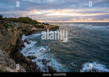 Die Sonne geht langsam über zerklüfteten Klippen auf, die entlang des Mahaulepu Heritage Trail in Koloa, Hawai, auf das raue türkisfarbene Wasser des Pazifischen Ozeans treffen Stockfoto