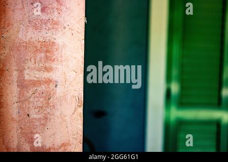 Orangefarbene Wand im Vordergrund, blaue Wand und grünes Fenster im Hintergrund geben einen schönen und farbenfrohen Vintage-Hintergrund-Effekt Stockfoto