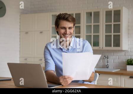 Glücklicher junger Geschäftsmann beim Lesen von Papier mit guten Nachrichten. Stockfoto