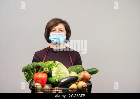 Eine Frau in einer OP-Maske, eine Europäerin mittleren Alters, eine Freiwillige, liefert Nahrung und Gemüse an die Bedürftigen während der Pandemie. Stockfoto