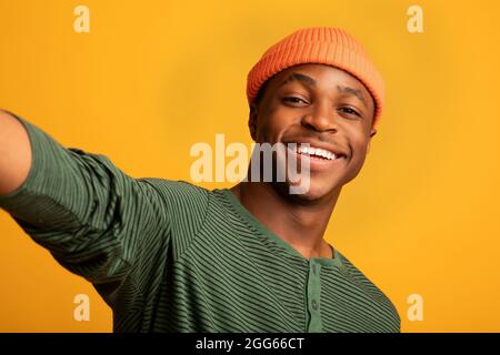 Happy Young Black Guy Nimmt Selfie Beim Posieren Über Yellow Studio Hintergrund Stockfoto