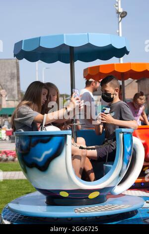 Jugendliche auf der Teetailfahrt im Sommer-Fayre, Helensburgh, Schottland, mit m obilen Telefonen und in einer Maske. Stockfoto