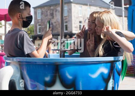 Jugendliche auf der Teetailfahrt beim Sommerfayre in Helensburgh, Schottland, mit Mobiltelefonen und in einer Maske. Stockfoto