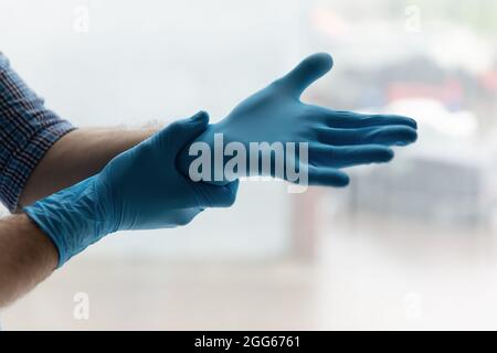 Hände eines Mannes, der blaue Latex-Gummihandschuhe aufsetzt Stockfoto