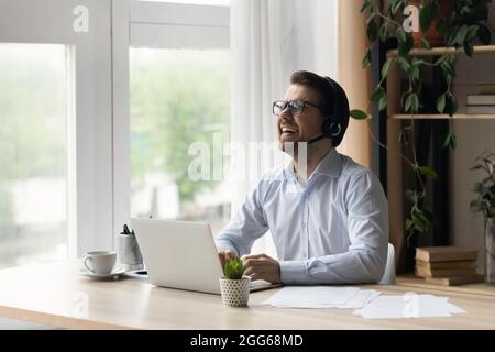 Glücklicher, begeisterter Geschäftsmann mit Kopfhörern, der am Laptop arbeitet Stockfoto