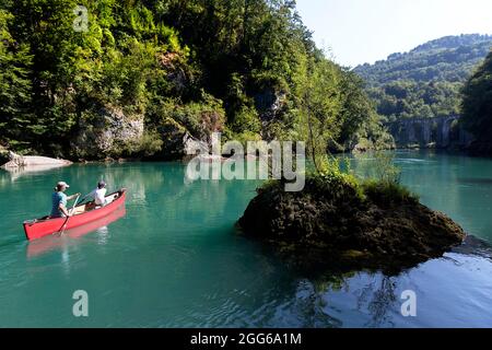 Mutter und Sohn rudern in einem roten Kanu auf dem Fluss Soca an einem überwucherten Felsen vorbei zu einer alten Steinbrücke in der Nähe von Most na Soci, Avce, Slowenien Stockfoto
