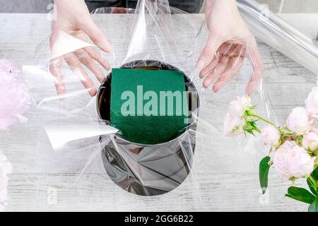 Florist bei der Arbeit: Wie man modische Blumenkachtel mit Pfingstrosen und Rosen macht. Schritt für Schritt, Tutorial. Stockfoto