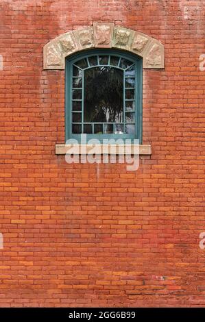 Kalifornische Kunst- und Handwerkskunst-inspiriertes Fensterdesign hoch oben in einer roten Backsteinwand. Stockfoto